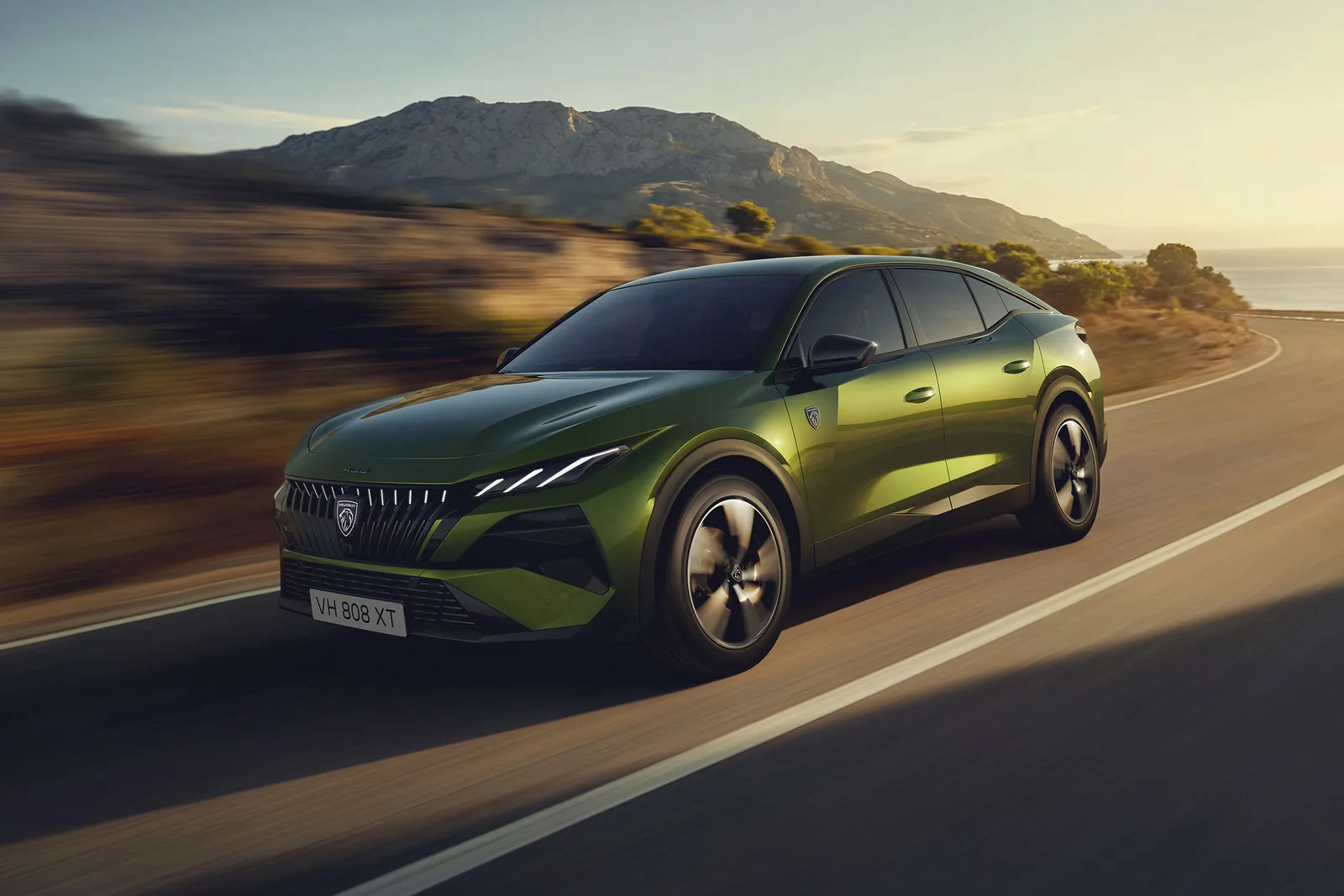 Peugeot 408 in green driving on a coastal road, the whole car visible