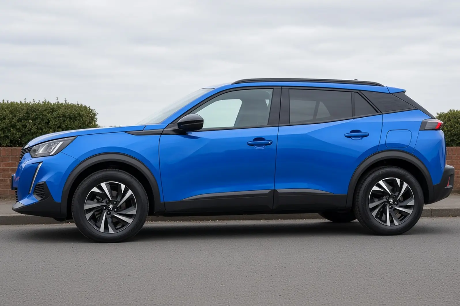 Peugeot 2008 second generation facelift in Vertigo Blue, side view on a British suburban street, the whole small SUV visible