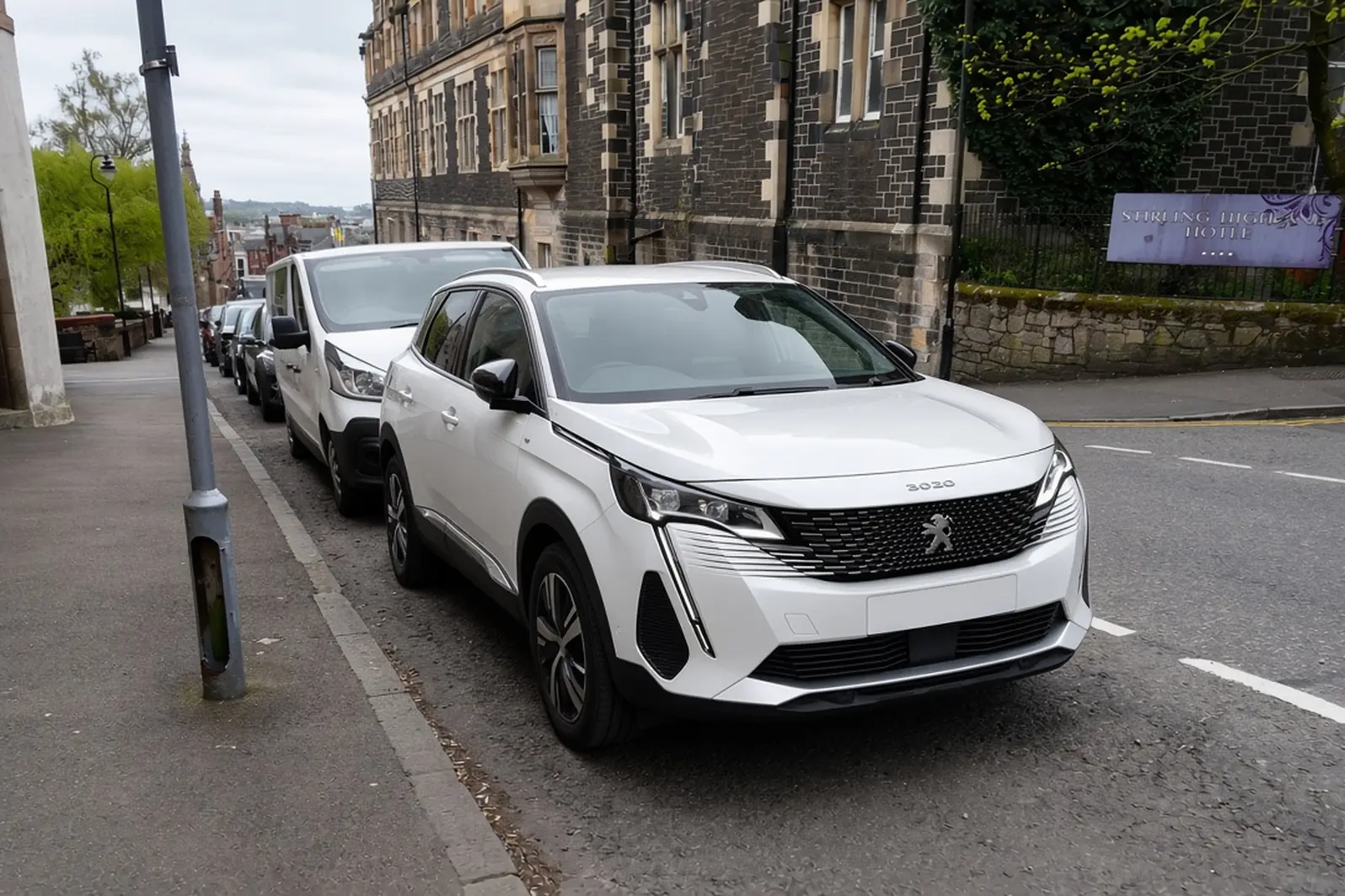 Peugeot 3008 second generation plug-in hybrid in Pearlescent White on a British town street, front three-quarter view, the whole SUV visible